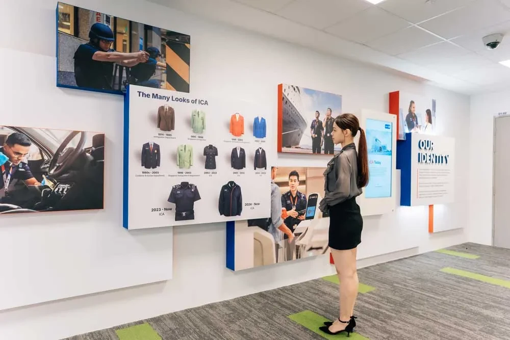 A wall of photographs of ICA officers, a display of uniforms called The Many Looks of ICA, and a panel called Our Identity, with a visitor looking on